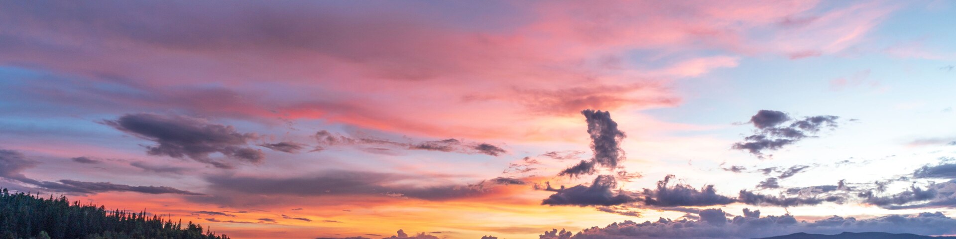 Ein ruhiger See spiegelt einen farbenprächtigen Sonnenuntergangshimmel wider, mit Bergen im Hintergrund.