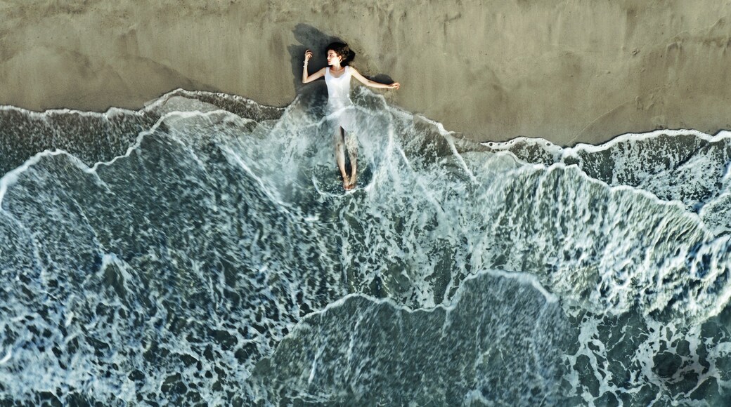 A person surfing on a wave with a sandy beach and a concrete wall in the background.