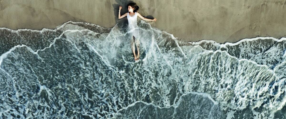 A person surfing on a wave with a sandy beach and a concrete wall in the background.