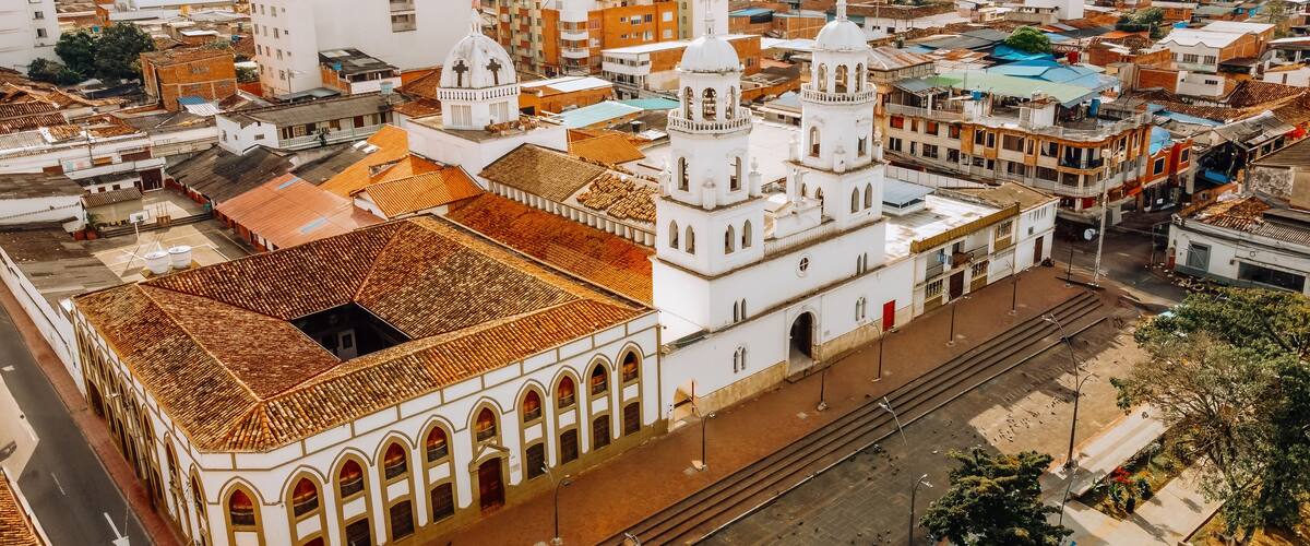 An aerial view of a city with a prominent white church with a dome and bell tower, surrounded by various buildings and a railway track.