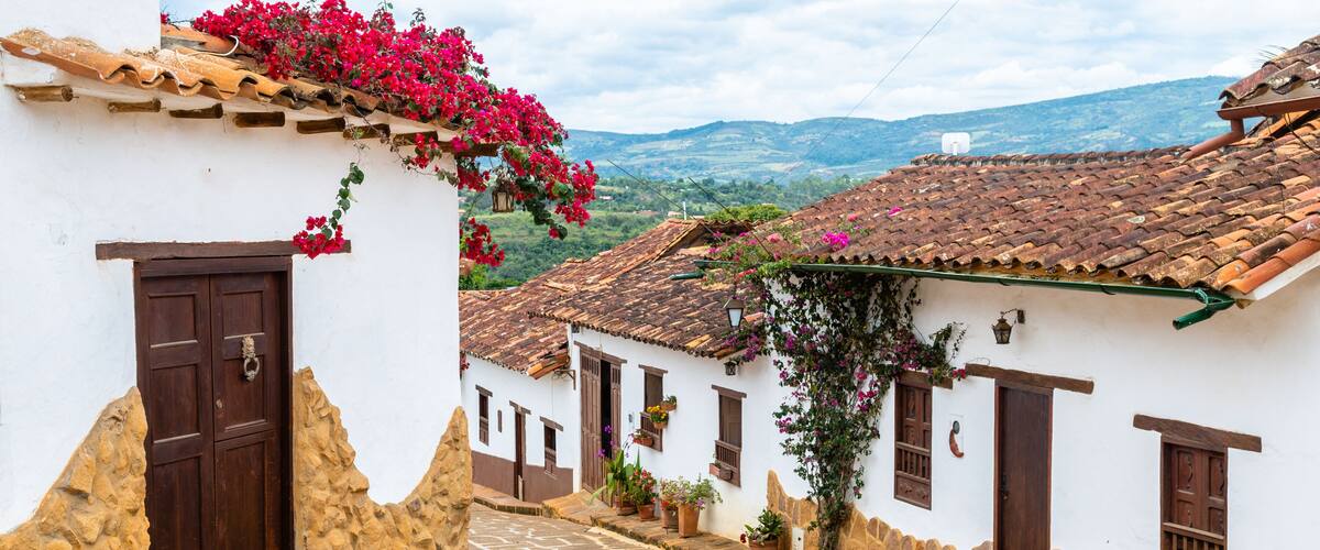 A cobblestone street with white buildings, red flowers, and a mountainous backdrop.