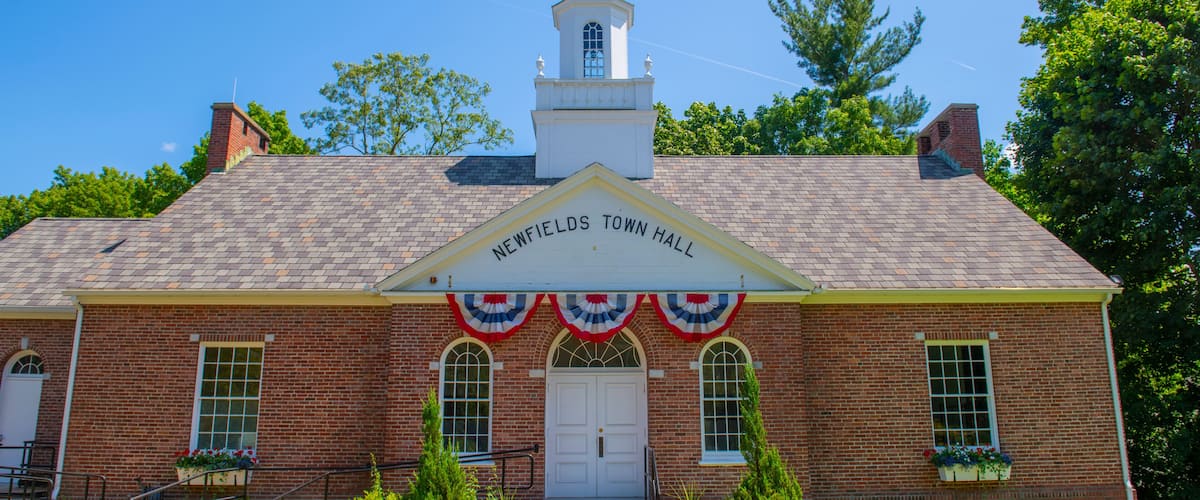 A brick building with a white steeple and a sign reading "Newfields Town Hall".