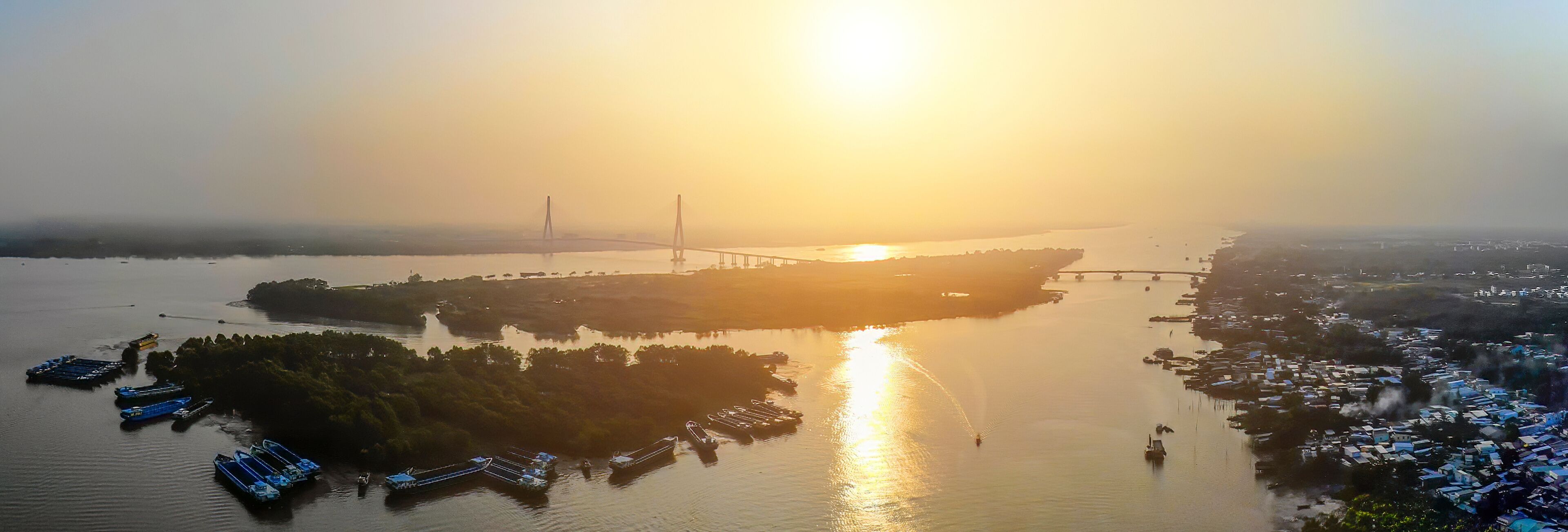A sunset over a river with a bridge and boats.
