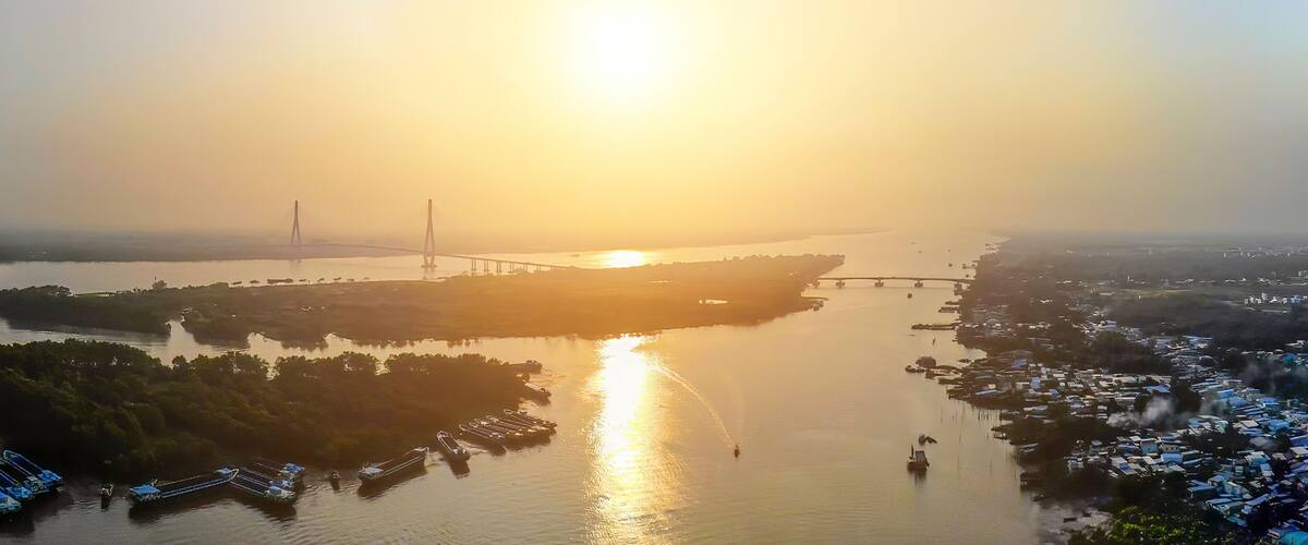 A sunset over a river with a bridge and boats.