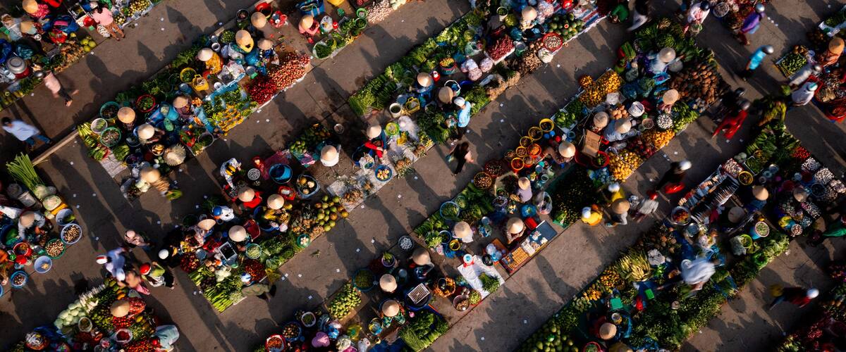 An aerial view of a bustling market with rows of vendors selling fruits, vegetables, and other goods.