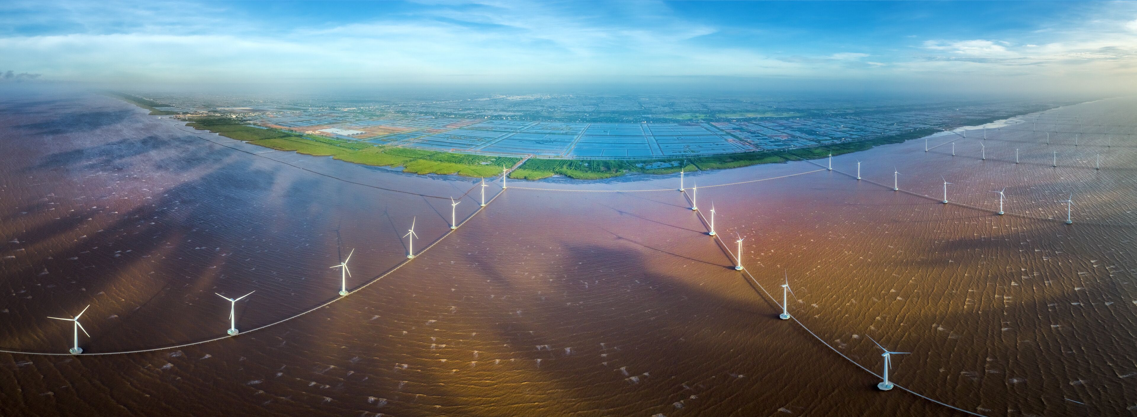 An aerial view of a coastal area with wind turbines and solar panels.