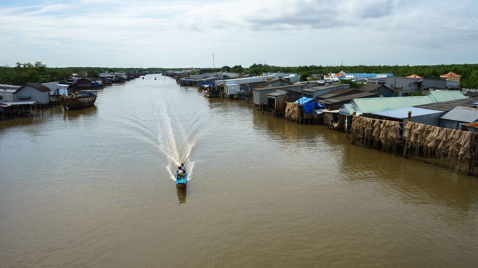 A river with houses on stilts and a boat creating a wake.