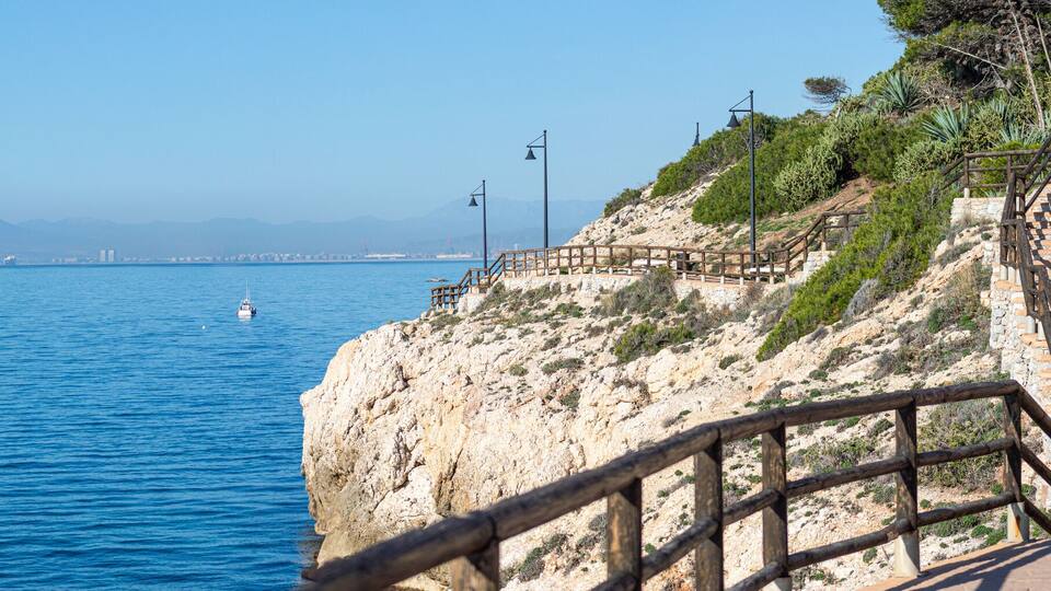 A coastal walkway with a view of the sea and distant mountains.