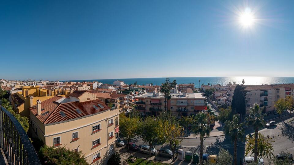 A coastal cityscape with a clear sky, a winding road, and a view of the sea.