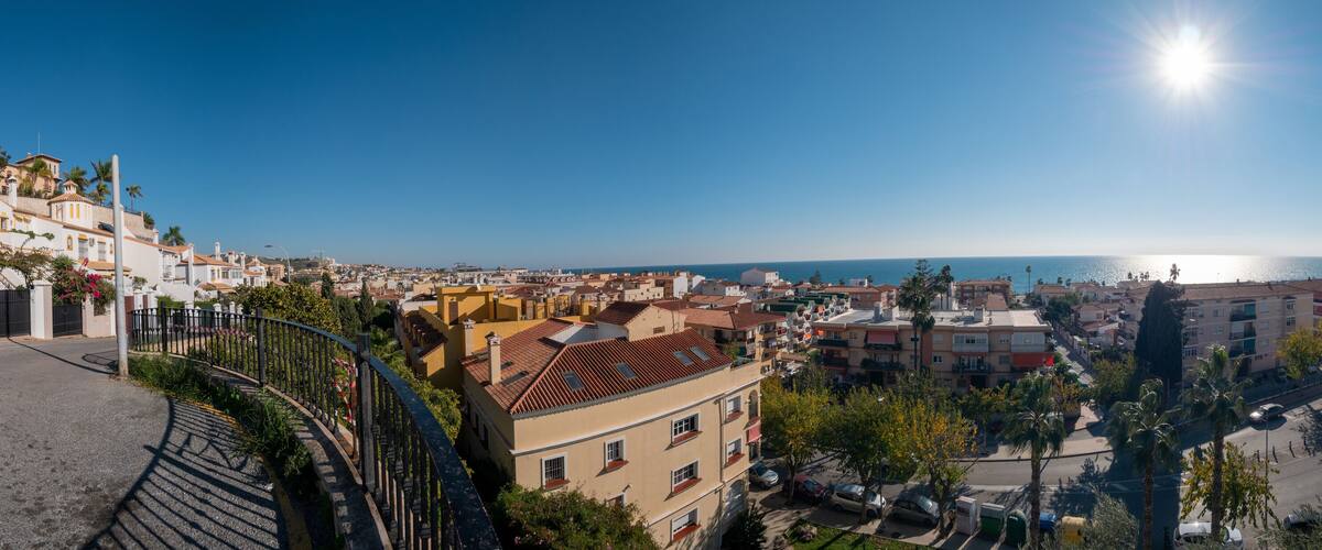 A coastal cityscape with a clear sky, a winding road, and a view of the sea.