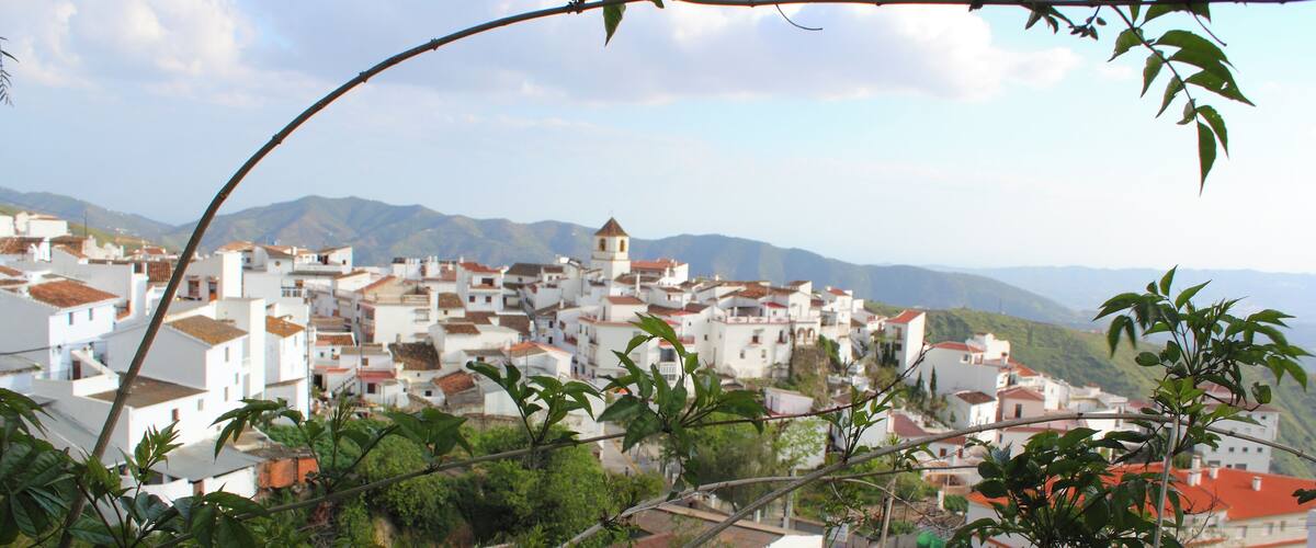 A coastal town with white buildings, a prominent church, and mountains in the background.