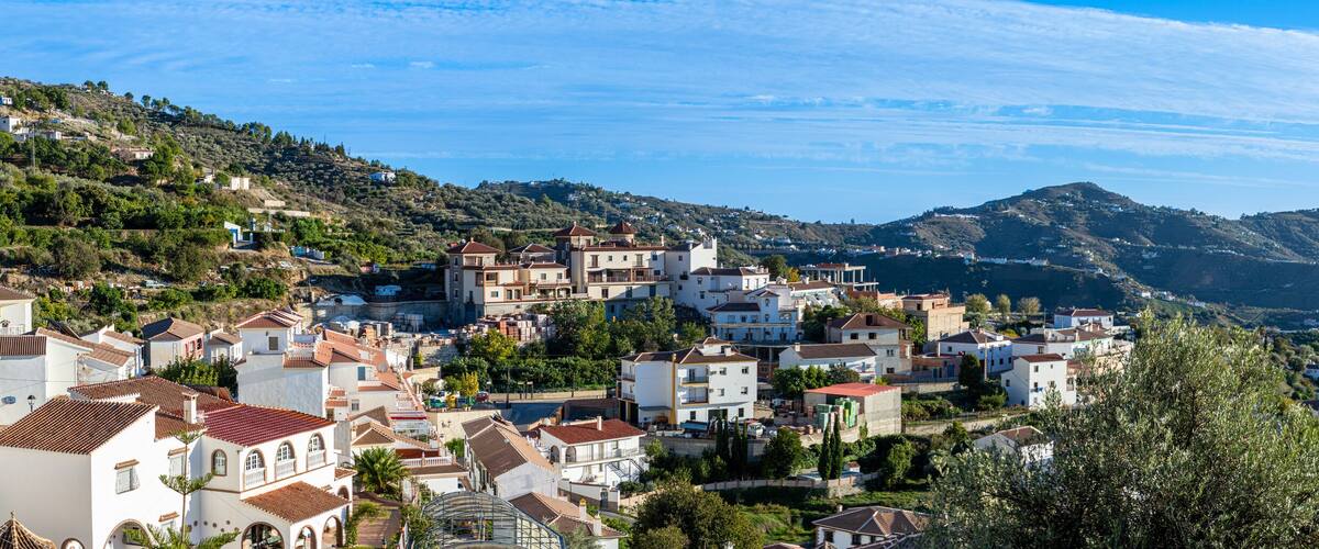 A hillside town with terracotta-roofed buildings, lush greenery, and a clear blue sky.