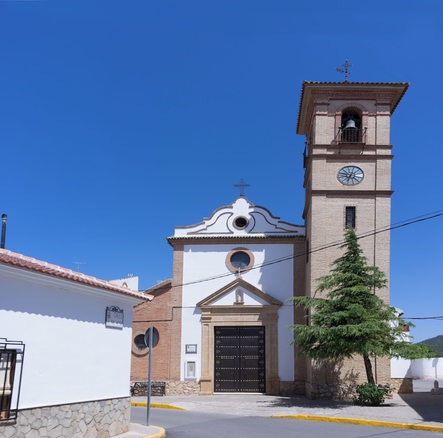 A church with a clock tower, a bell, and a cross on top.