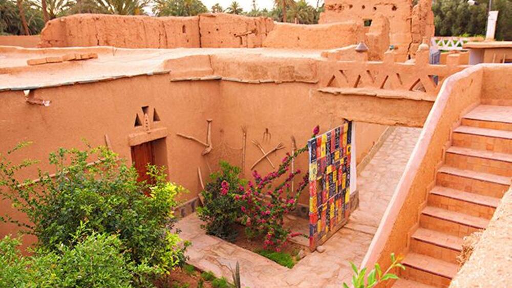 Un bâtiment traditionnel en briques de terre crue, doté d’un escalier et d’une tapisserie colorée suspendue à un balcon.