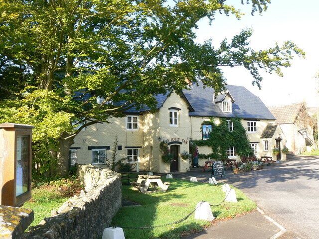 A traditional stone building with a sign reading "The Old Mill Inn" surrounded by greenery and a stone wall.