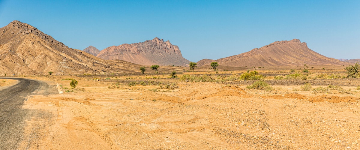 A desert landscape with a winding road, sparse vegetation, and two prominent mountains.