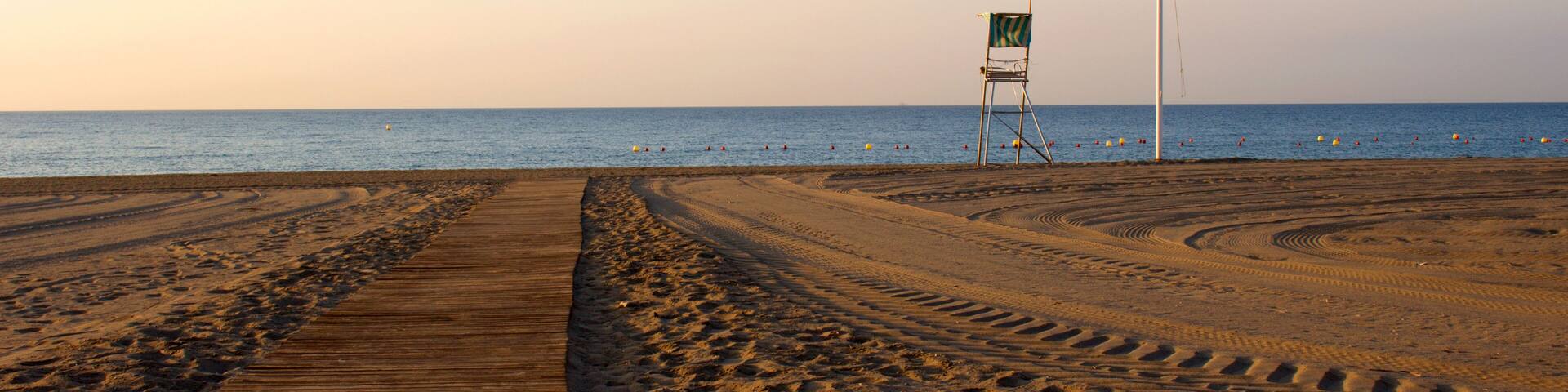 A beach with a wooden boardwalk, footprints, and a lifeguard chair.