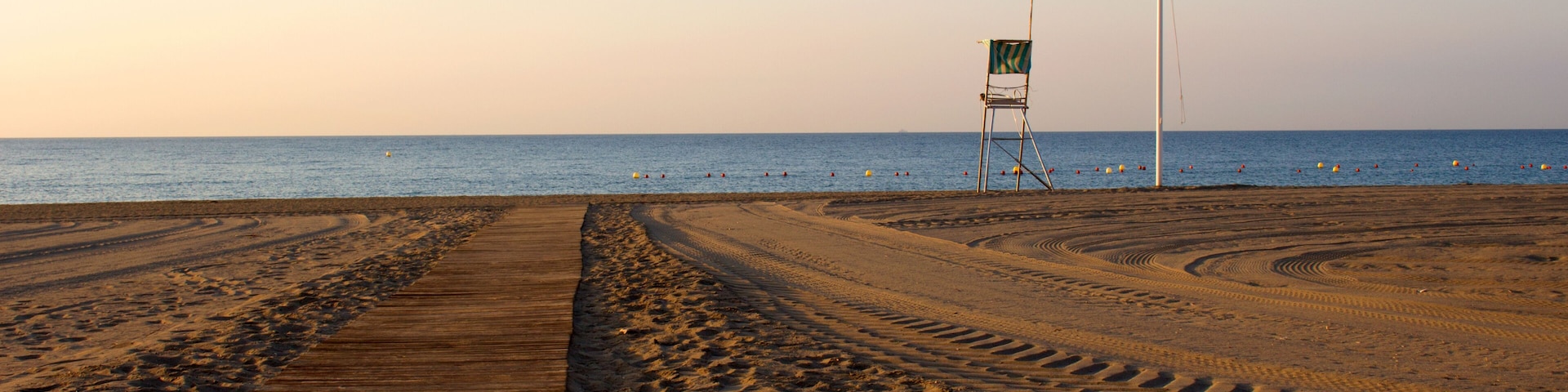 Ein Strand mit einer Holzpromenade, Fußabdrücken und einem Rettungsschwimmerstuhl.