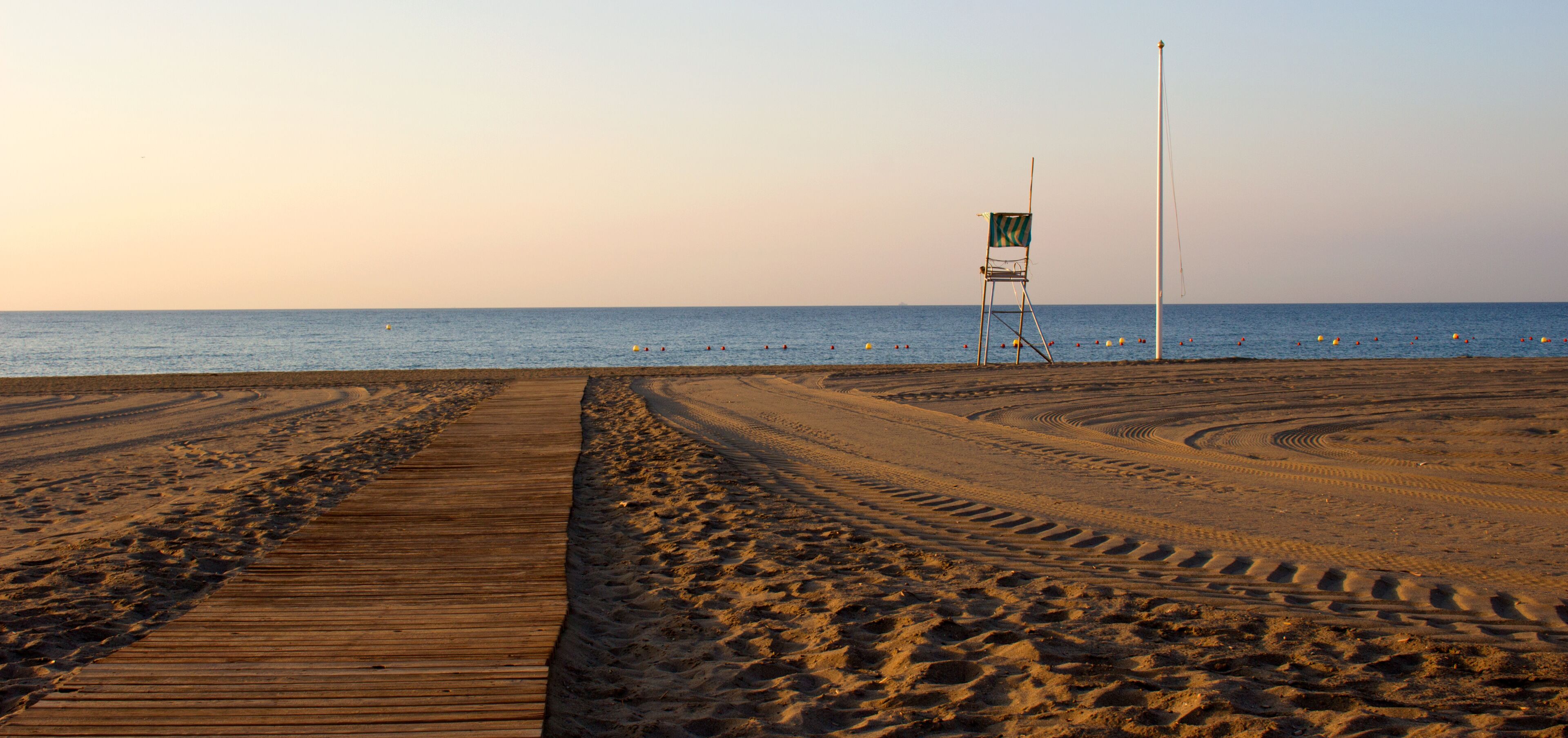 A beach with a wooden boardwalk, footprints, and a lifeguard chair.