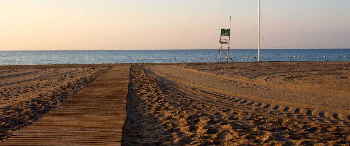 A beach with a wooden boardwalk, footprints, and a lifeguard chair.