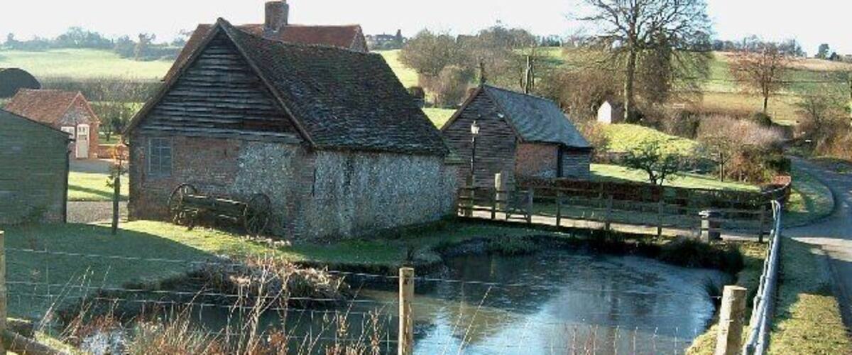 A rural waterway with old stone buildings and a wooden bridge.