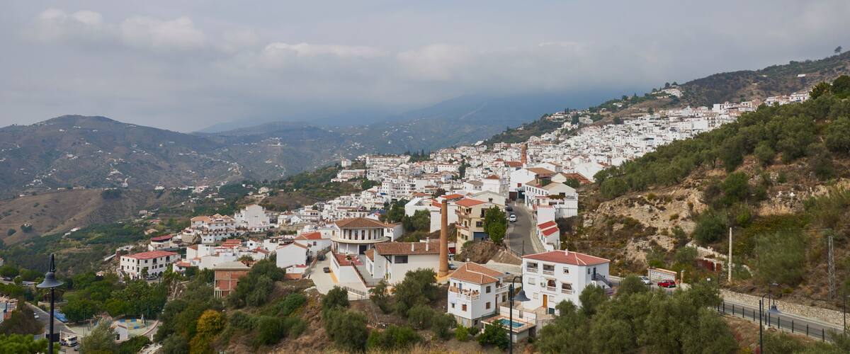 A coastal town with white buildings, a prominent church tower, and a winding road.