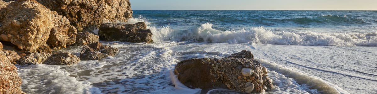 A rocky beach with waves crashing onto the shore and a clear blue sky.