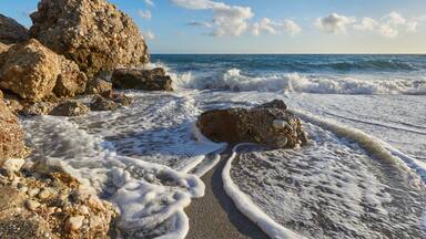 A rocky beach with waves crashing onto the shore and a clear blue sky.