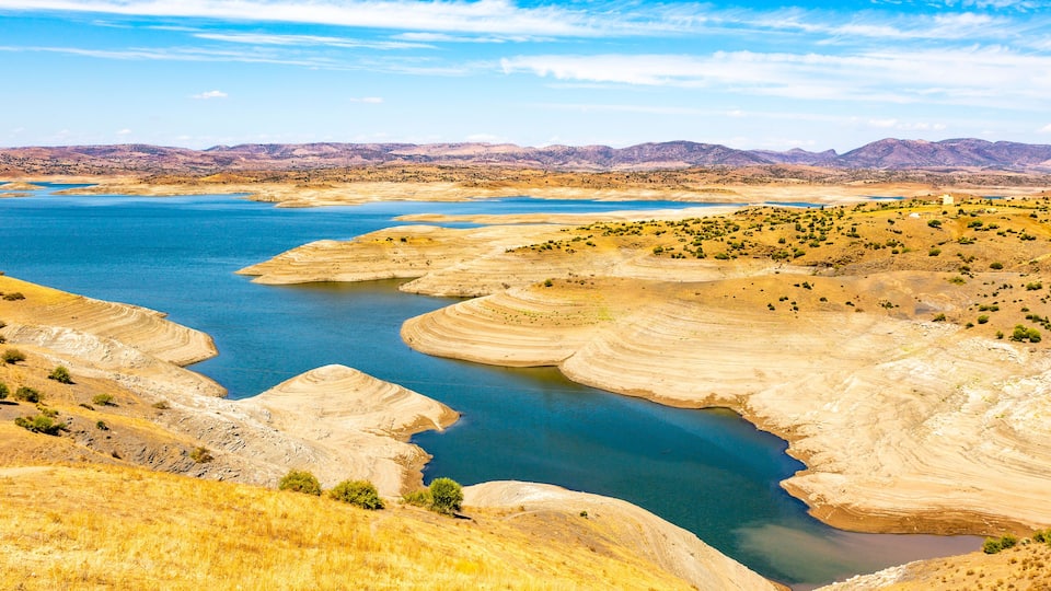 A large river with surrounding dry, hilly terrain and distant mountains.