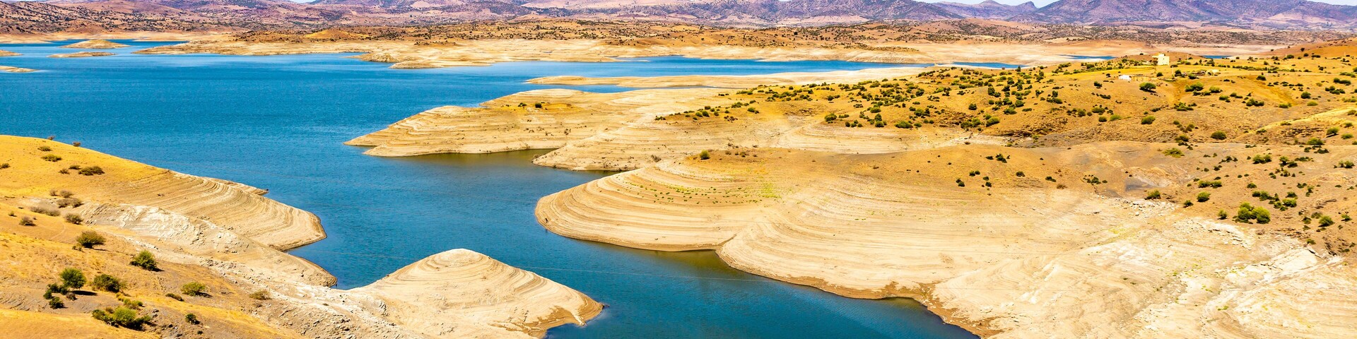 Un río caudaloso rodeado de terreno seco y montañoso, con montañas a lo lejos.