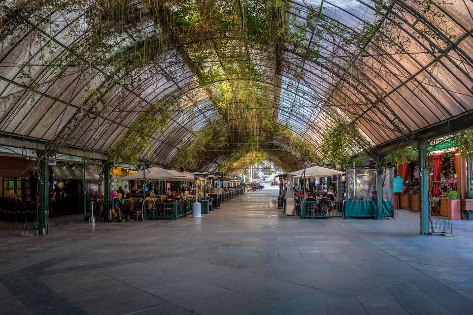 Mercado interior con techo de vidrio, puestos a ambos lados y un pasillo central.