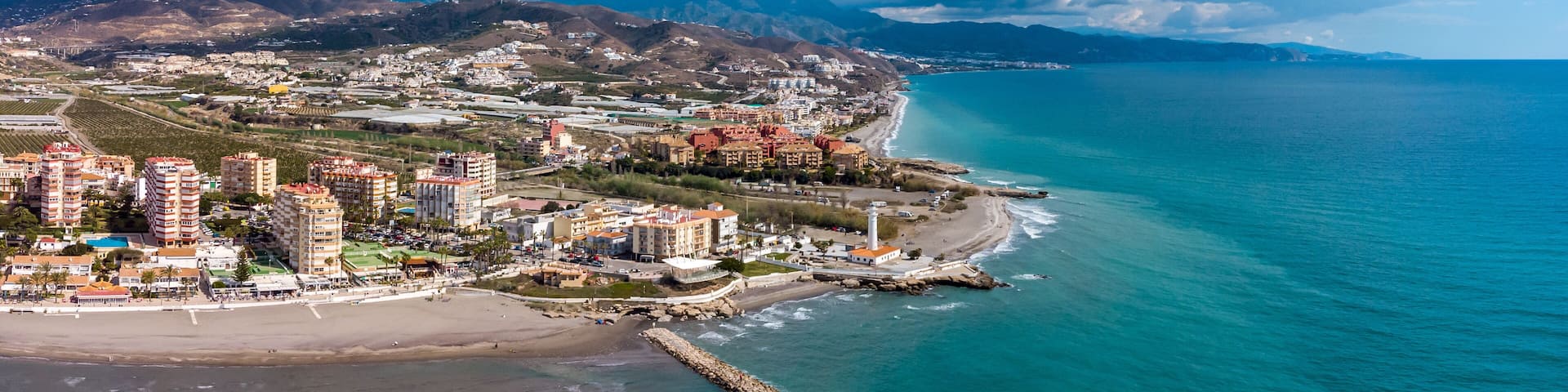 Drone perspective of costal city of Torrox situated in Malaga, Costa del Sol, Spain. Touristic travel destination. View of the promenade and beach area. The lighthouse of Torrox and the river.