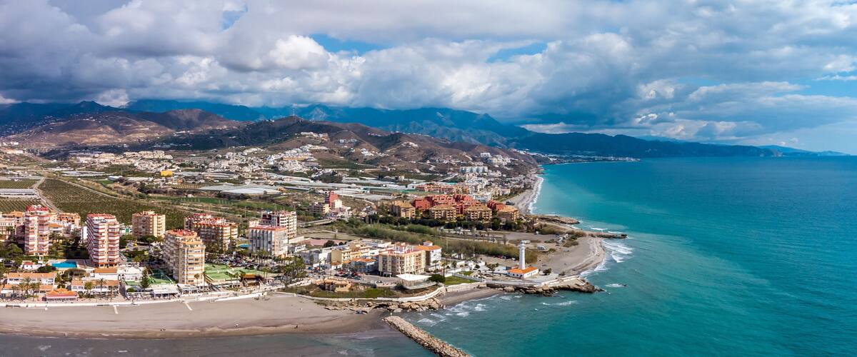 A coastal town with a beach, buildings, and mountains in the background.