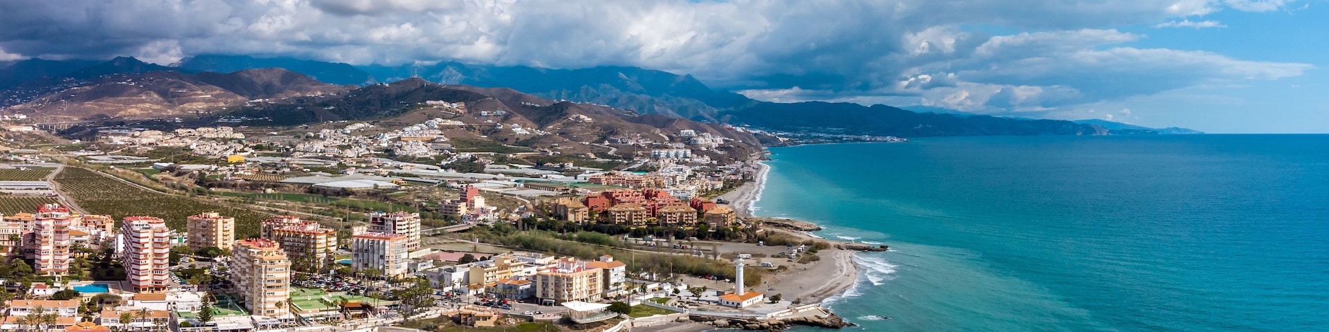 A coastal town with a beach, buildings, and mountains in the background.