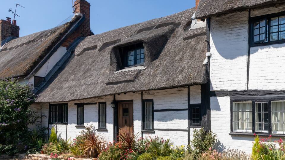 A traditional white house with a thatched roof and black window frames.