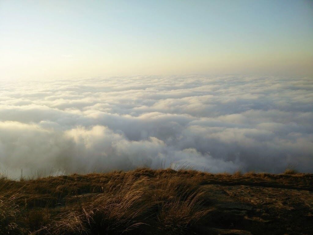 Une vaste étendue de nuages s’étend sous un coteau verdoyant.
