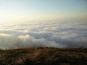 A vast sea of clouds below a grassy hilltop.