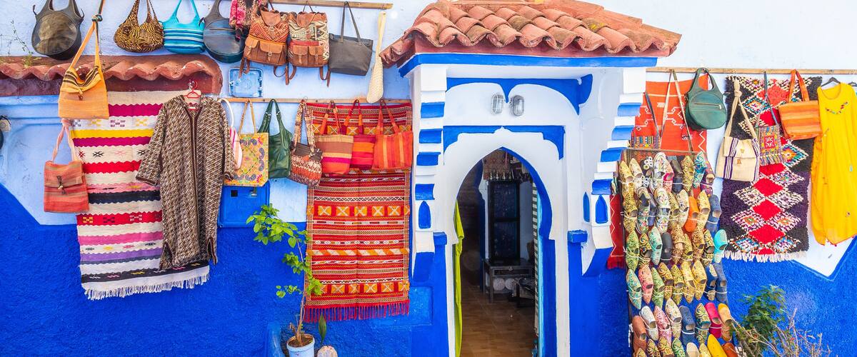 A colorful shop with various bags, shoes, and textiles displayed outside.