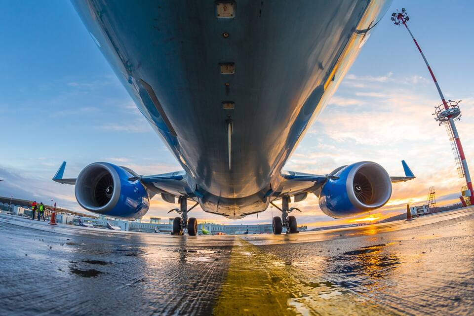 An airplane on a wet runway with a sunset in the background.
