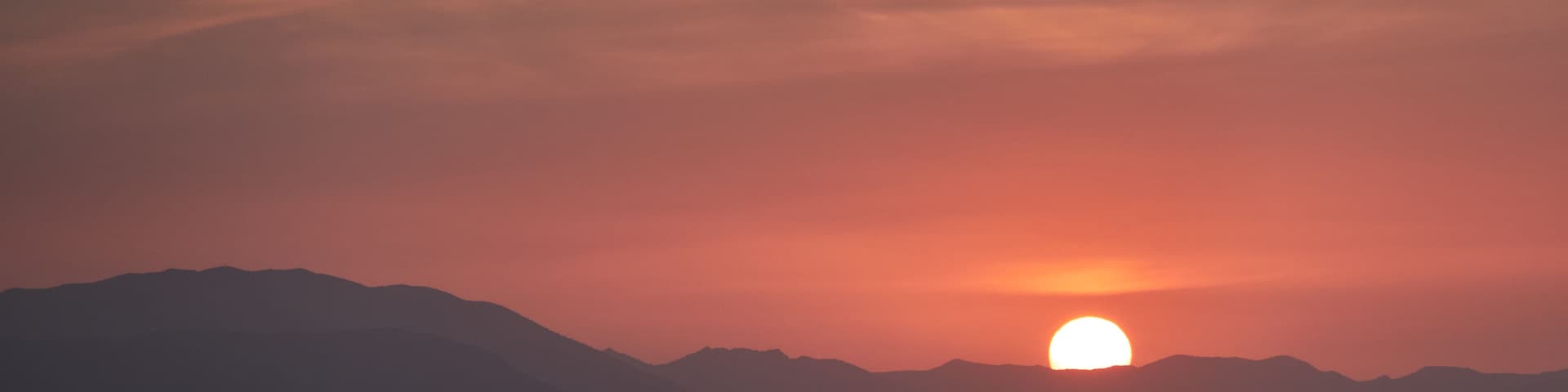 A sunset over a beach with waves and mountains in the background.