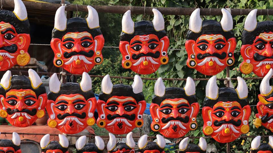 A collection of colorful masks with horns and mustaches hanging on a wire.