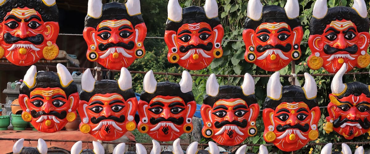 A collection of colorful masks with horns and mustaches hanging on a wire.