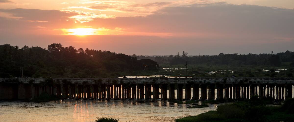 A sunset over a river with a bridge and trees in the background.
