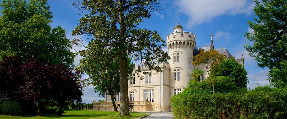 A castle with a tower, surrounded by trees and a gravel path.