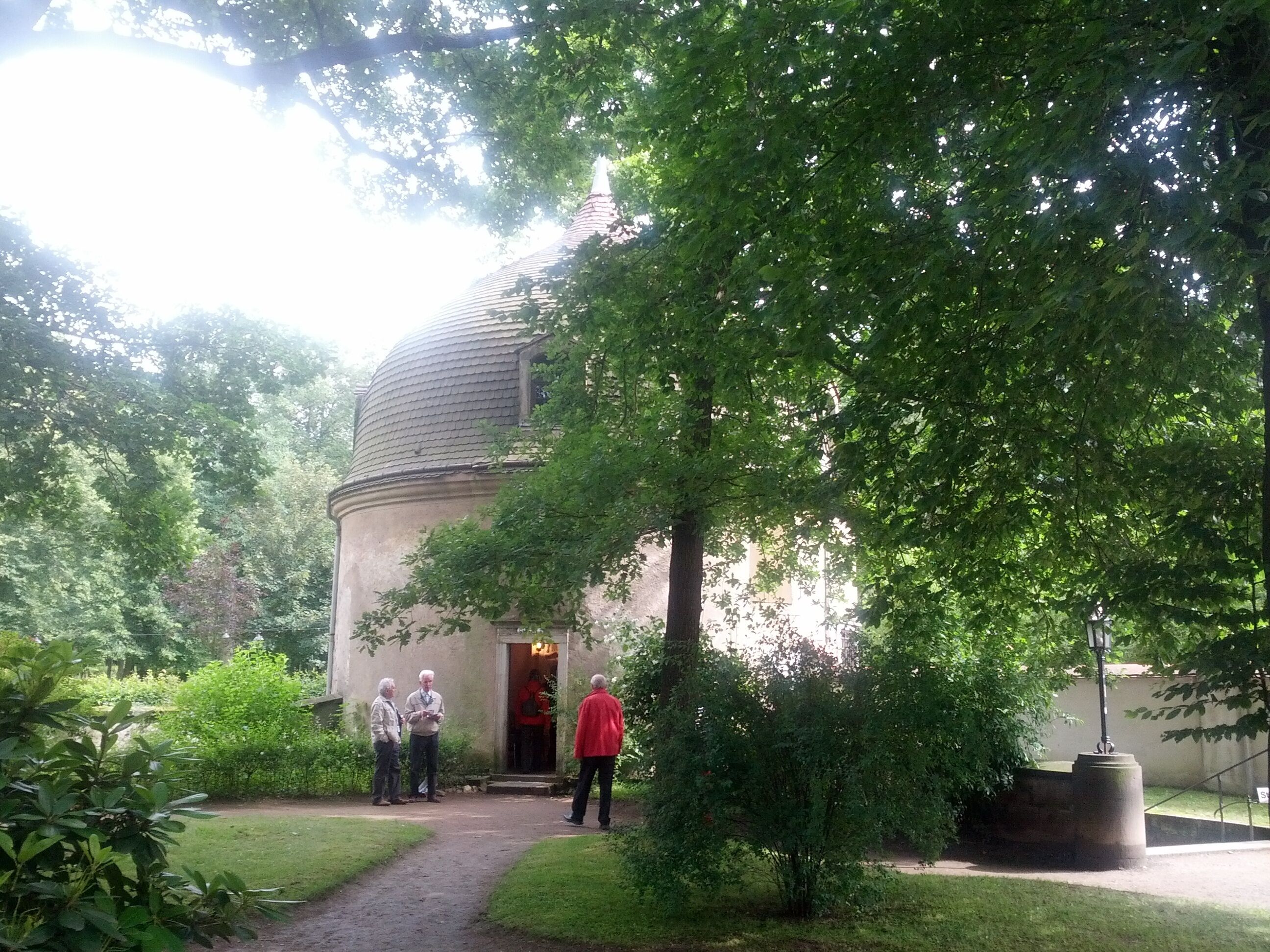 A historic building with a dome, surrounded by lush greenery and a pathway.
