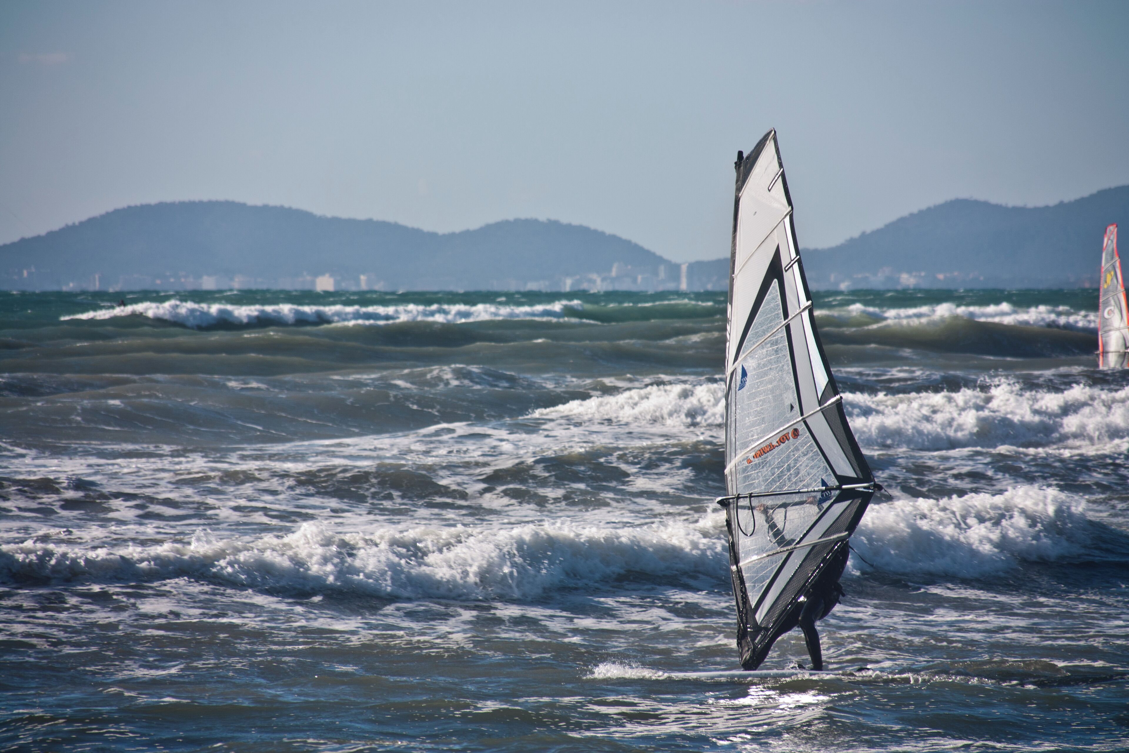 A windsurfing board in the ocean with waves and a distant mountain range.