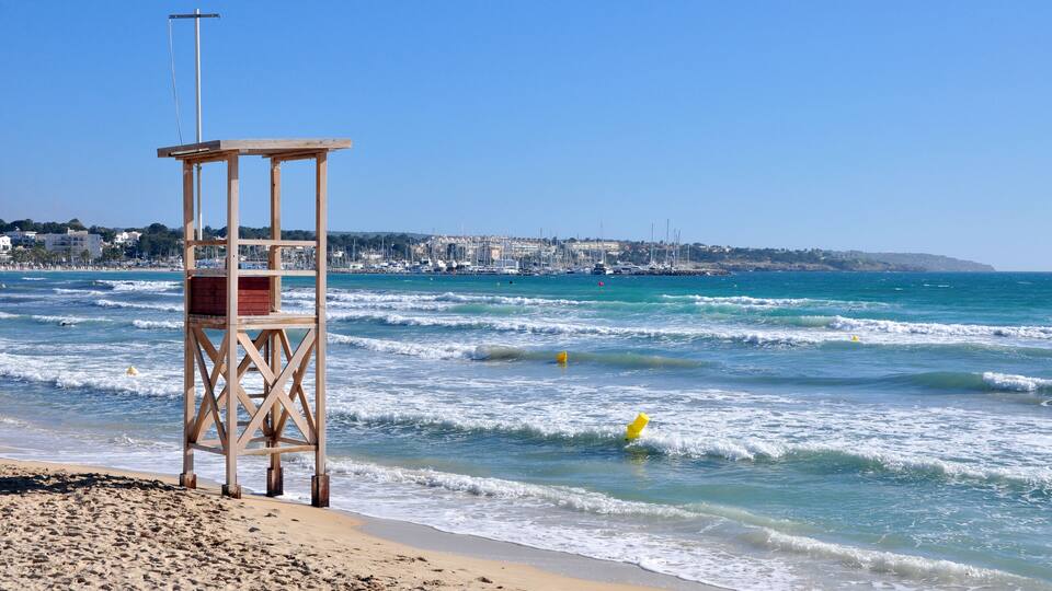 A wooden lifeguard tower on a sandy beach with waves crashing onto the shore.