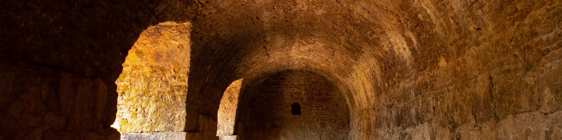 Um corredor de pedra arqueado com paredes rústicas e chão empoeirado.