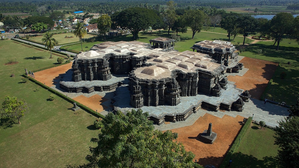 Aerial view of the ancient, elaborately carved Ishvara Temple complex standing majestically amidst lush greenery, Arasikere, Karnataka, India.