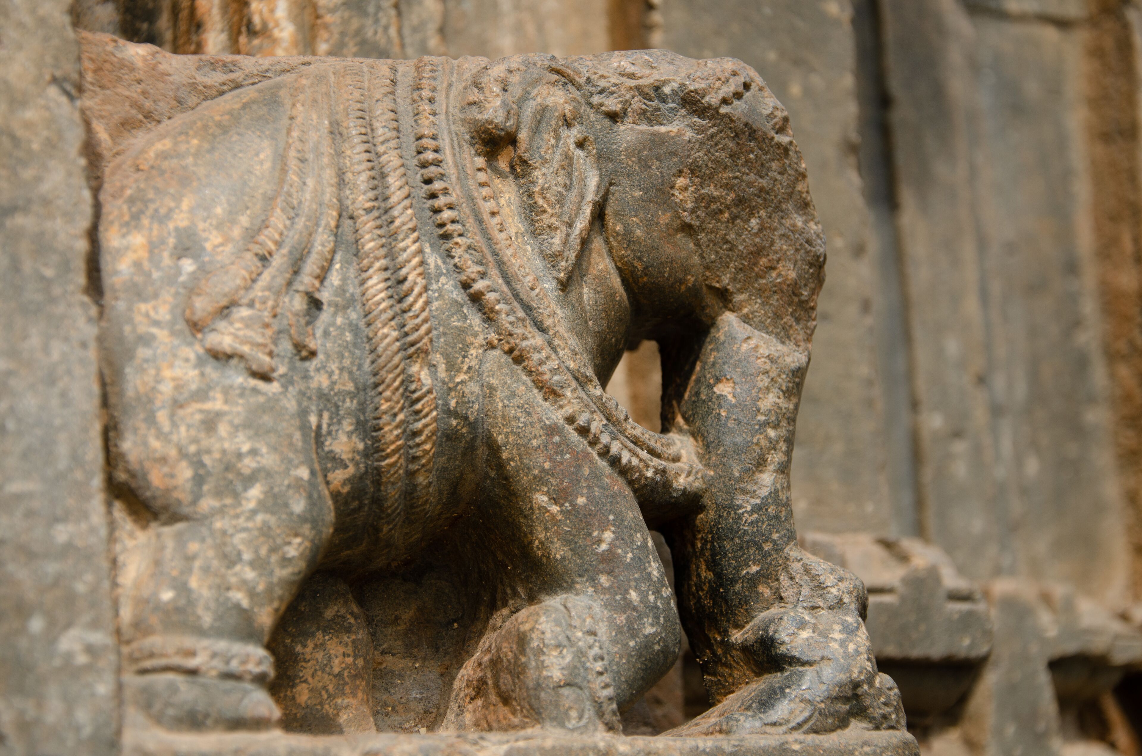 A weathered stone elephant sculpture with intricate carvings and a rope around its neck.